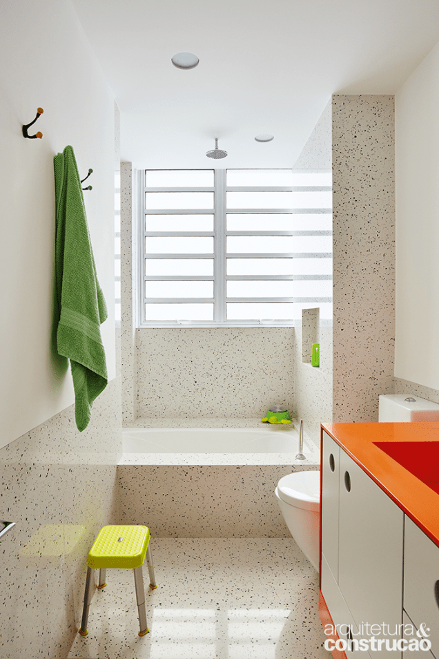 Para o ambiente das crianças,os arquitetos escolheram uma bancada de Corian laranja e revestiram meia-parede e piso de um padrão de Silestone que lembra o granilite original do apartamento.