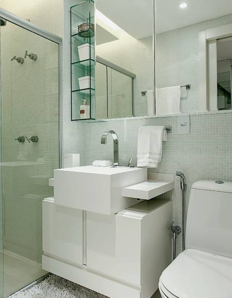 Com apenas 3 m²,  o banheiro íntimo foi vestido inteiramente de branco, medida que evitou a sensação de clausura e ainda deu à área uma atmosfera elegante. O projeto de estilo  clean soma pastilhas de vidro, bancada de silestone e mobiliário sob medida. “Projetamos o gabinete inferior menos profundo do que a cuba para criar a ideia de movimento. Essa é uma ótima pedida para ambientes pequenos”,justifica o arquiteto. Mais fininho ainda (com apenas 12 cm de profundidade), o armário suspenso é revestido de espelhos e ladeado por prateleiras de vidro, que, com sua transparência, contribuem para a fluidez da ambientação. Projeto d<span>o arquiteto paulista </span><span>Thiago Manarelli</span><span> e da designer de interiores pernambucana </span><span>Ana Paula Guimarães.</span>