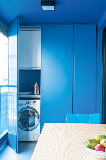 Uma das extremidades do terraço comporta a lavanderia, dentro do nicho de 0,80 x 1 x 2,60 m fechado com portas laqueadas de azul, tom próximo ao teto original do ambiente. Sim, a área de serviço do apartamento se resume à máquina de lavar e aos armários de MDF laminado para os utensílios. Há ainda bancada, tanque e vassouras.