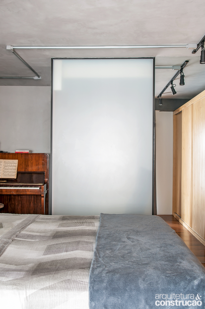 Até o piano dos moradores encontrou lugar entre sala e quarto. Toda a elétrica fica aparente no forro de cimento queimado, exposta em tubos de aço galvanizado. O banheiro se localiza atrás do painel. Sem janelas, o cômodo pedia luz natural, obtida graças a esta divisória de vidro jateado (Roberto Jerônimo Vidraceiro). Com 1,05 x 2,60 m e 1 mm de espessura, ela está fixada em caixilhos de alumínio com pintura eletrostática preta.