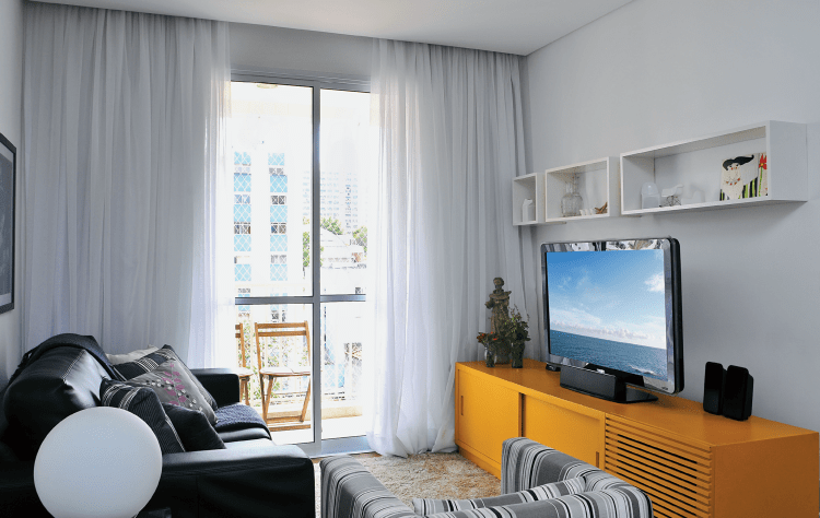 <span>Desenhado por Renata, o rack laqueado de amarelo tem portas deslizantes e um compartimento ripado para o subwoofer do home theater. </span>Projeto da designer de interiores Renata Marré