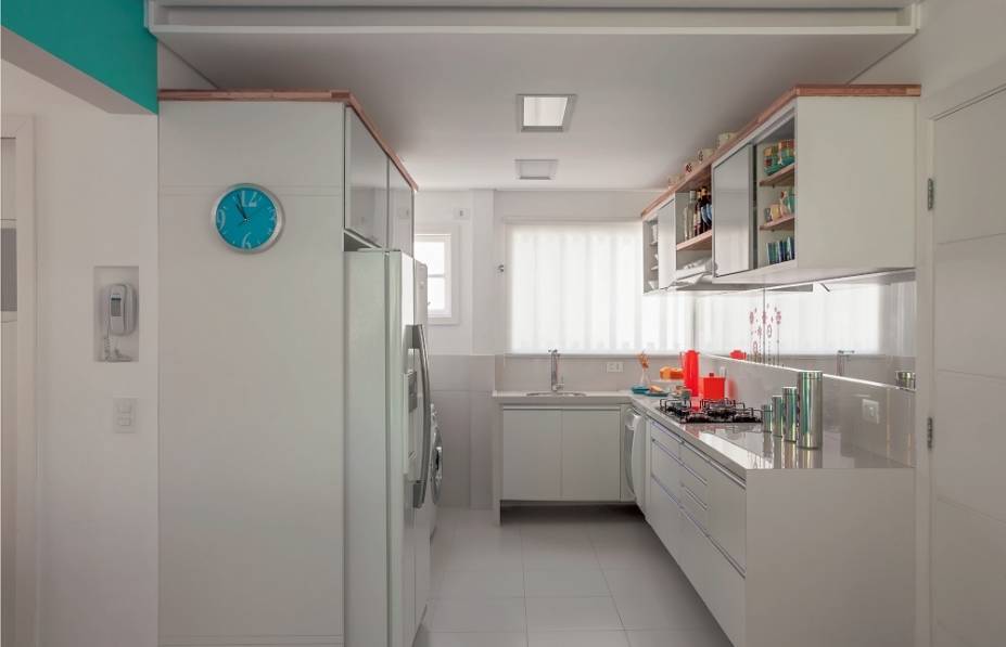<span>Os armários da cozinha foram projetados pela arquiteta Gina de Paulo, que especificou como material dominante o MDF revestido de laminado branco brilhante. De modo a incrementar a marcenaria, há prateleiras de teca e portas superiores de vidro branco basculantes ou de correr. Projeto da arquiteta Gina de Paulo, do Idea Estúdio.</span>