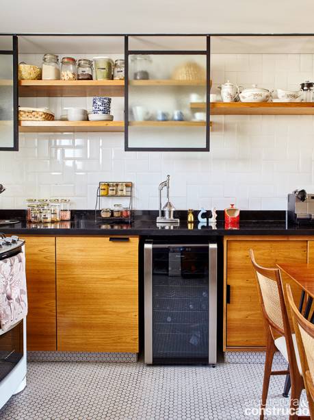A cozinha tem bancadas de granito preto absoluto (Pedras Marajoara Marmoraria) acima dos armários de freijó. Com 80 cm de altura, o painel de vidro jateado em caixilho de aço corre no trilho superior, compondo arranjo com as prateleiras.