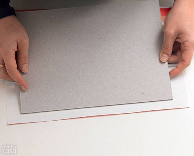 1. Sobre o verso do recorte maior de Con-Tact, apoie um dos papéis holler de 20,5 x 27 cm (que será a capa), deixando uma sobra de 2,5 cm em três das laterais. Comece a puxar a película do adesivo e cole um pequeno trecho.