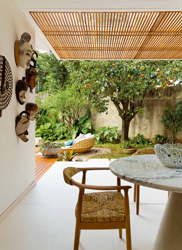 Um pergolado metálico com ripas de freijó fornece sombra ao cantinho voltado para o quintal (onde desponta, ao fundo, o pé de caqui). O espaço conta com churrasqueira e fica anexo à sala de jantar. Um pergolado metálico com ripas de freijó fornece sombra ao cantinho voltado para o quintal (onde desponta, ao fundo, o pé de caqui). O espaço conta com churrasqueira e fica anexo à sala de jantar.