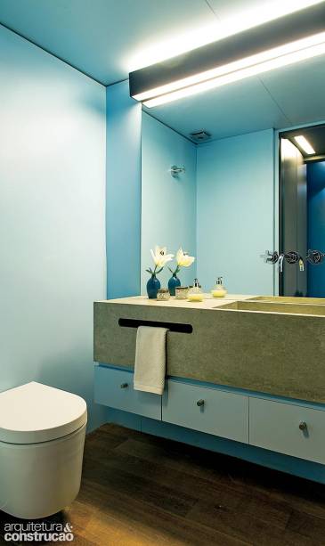 Aplicado sobre drywall em todo o espaço, o laminado melamínico descomplicou a obra deste banheiro. Sem rejuntes e adotado também na marcenaria, ainda colaborou para o visual homogêneo. Nos trechos secos, as placas se estendem do forro ao piso – no boxe, a arquiteta Fabiana Stuchi, do Stuchi & Leite Projetos, preferiu o Formiwall (Formica) e fez o acabamento inferior com o mesmo porcelanato da cuba. A peça foi montada sob encomenda com unidades de 60 x 120 cm (linha Concretissyma, da Portobello) e ganhou no recorte (3) um discreto pendurador de toalhas.