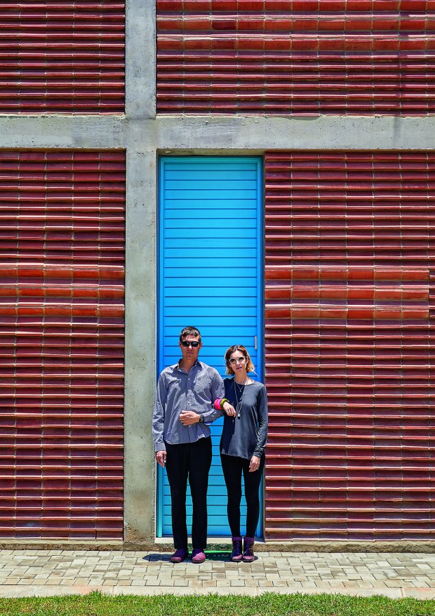 Os donos da casa, o arquiteto Gregory Katz e sua esposa, Caryn, à frente da fachada de tijolo chanfrado: a disposição das peças para umlado e para o outro conseguiu o resultado ondulado incomum. O azul-mediterrâneo escolhido para a porta de entrada exibe estudado contraste.