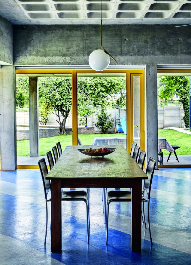 A sala de jantar, coroada pelo pendente da Flos, olha para o jardim. A transição para a área externa se dá numa espécie de varanda, elemento comum nas casas da África do Sul. Portas de correr de alumínio pintado com vidro duplo.