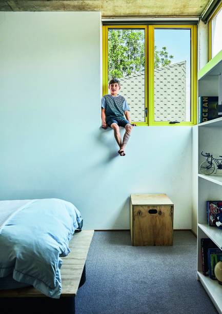 Um dos filhos do casal, Zackary, posa na janela extra-alta de seu quarto, diante das esquadrias de alumínio pintadas de amarelo – e devidamente fechadas. “Essa opção aproxima os moradores das copas das árvores”, justifica Gregory.