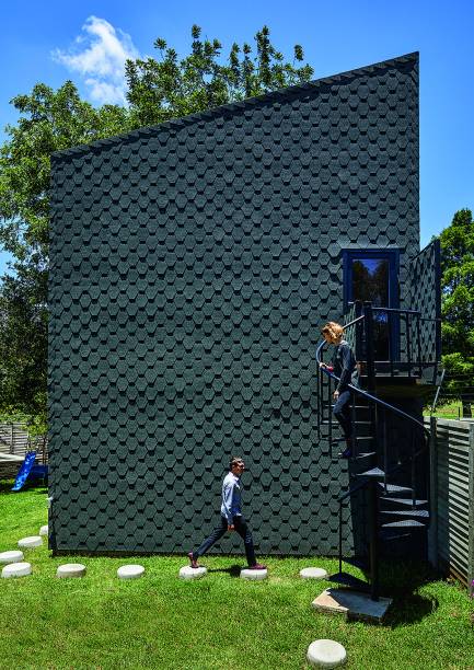 Comumente aplicada na cobertura, a telha shingle (base asfáltica, com 2 mm de espessura) cobre todo o exterior do anexo-escritório, erguido com estrutura de aço. Para durar mais, ela recebeu uma camada protetora de silicato.