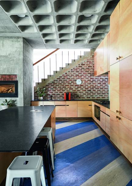Teto de toda a casa assume a laje nervurada em sua aparência original, revelando a abordagem prática e crua da arquitetura. Na marcenaria da cozinha, chapas de compensado.