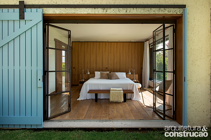 Acordar olhando para a paisagem é a proposta do quarto do casal. Também pintada de azul (Suvinil, ref. D076), a porta exterior de 2,35 x 3,18 m corre em trilhos de ferro aparentes. Manta e almofada da Luhome.