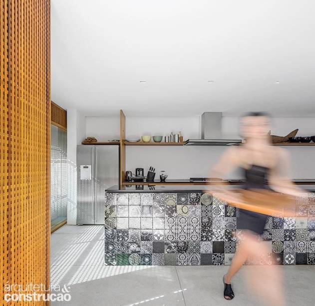 Junto da área social, fica a cozinha, voltada para o ambiente de jantar e contida num volume de madeira que comporta também a lavanderia e o lavabo. Bancada com azulejos de Calu Fontes.