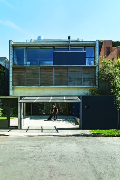 A fachada revela a ocupação vertical do terreno: garagem no térreo, quartos no primeiro pavimento (fechados com painéis ripados de cumaru), estar logo acima (parte envidraçada) e, por fim, a cobertura, grande terraço aberto para o panorama conquistado com a posição alta do lote.