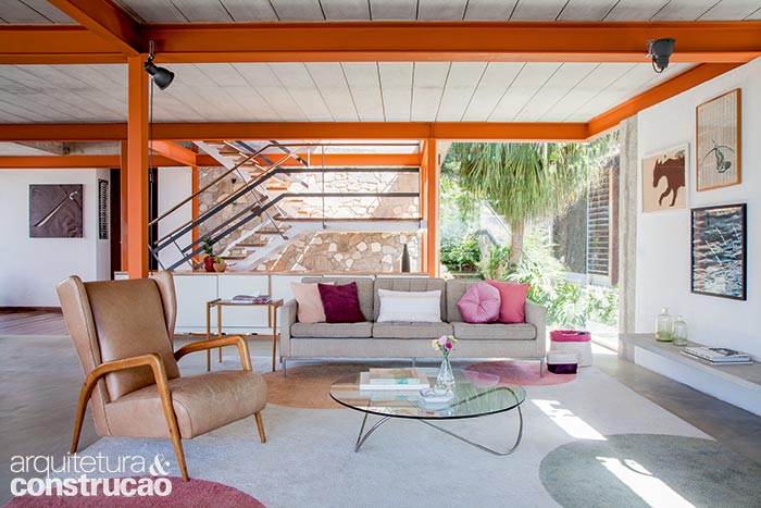 Na sala de estar, as lajes aparentes de concreto pré-moldado formam par com a estrutura metálica pintada de laranja. A parede atrás da escada exibe escombros da antiga construção convertidos em concreto ciclópico. As almofadas, a mesa de centro e os revisteiros são da Futon Company. Projeto de Rafic Farah. Na sala de estar, as lajes aparentes de concreto pré-moldado formam par com a estrutura metálica pintada de laranja. A parede atrás da escada exibe escombros da antiga construção convertidos em concreto ciclópico. As almofadas, a mesa de centro e os revisteiros são da Futon Company. Projeto de Rafic Farah.