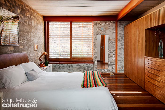 A suíte principal é o cômodo mais próximo da rua e uma miniescotilha junto à cama deixa ver as visitas lá fora. As paredes internas foram mantidas sem acabamento para valorizar a aparência bruta do concreto ciclópico. A suíte principal é o cômodo mais próximo da rua e uma miniescotilha junto à cama deixa ver as visitas lá fora. As paredes internas foram mantidas sem acabamento para valorizar a aparência bruta do concreto ciclópico.