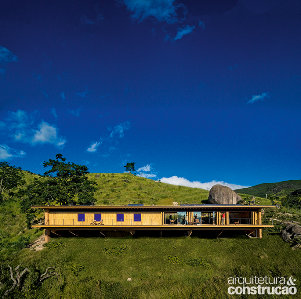 As janelinhas azuis são folhas de correr revestidas de laminado: a cor é uma homenagem às casas coloniais. Nesta foto, é possível notar a forte inclinação do terreno, de 20 graus. Uma grande rocha, ao fundo, à dir., foi mantida: contraponto ao desenho retilíneo minimalista.