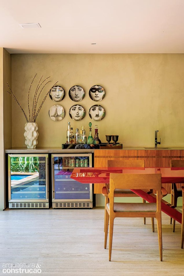 Na sala de jantar, o balcão com tampo de inox (Mekal) acomoda adega, frigobar, pia e um cooktop com coifa retrátil.