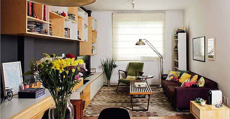 <span>Cômodo mais usado do apartamento, a sala foi o ponto de partida da renovação. Para ocupar sua parede mais extensa, o arquiteto </span><span>Gustavo Capecchi </span><span>desenhou um móvel multifuncional – composto por diversos módulos,  ele atua como bar, mesa de refeições, rack, escrivaninha e estante, além de acomodar taças, eletrônicos e até um colchão inflável para visitas. </span>