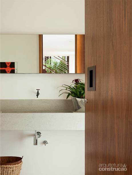 No lugar da maçaneta comum, a cava de aço corten inserida na porta de nogueira pivotante já revela o zelo da arquiteta Paula Bittar pelos detalhes. Na bancada e no piso, ela optou pelo limestone baiteg blue. “É bem decorativo, mas, como pede impermeabilização para evitar marcas de água, só uso em lavabos”, conta.