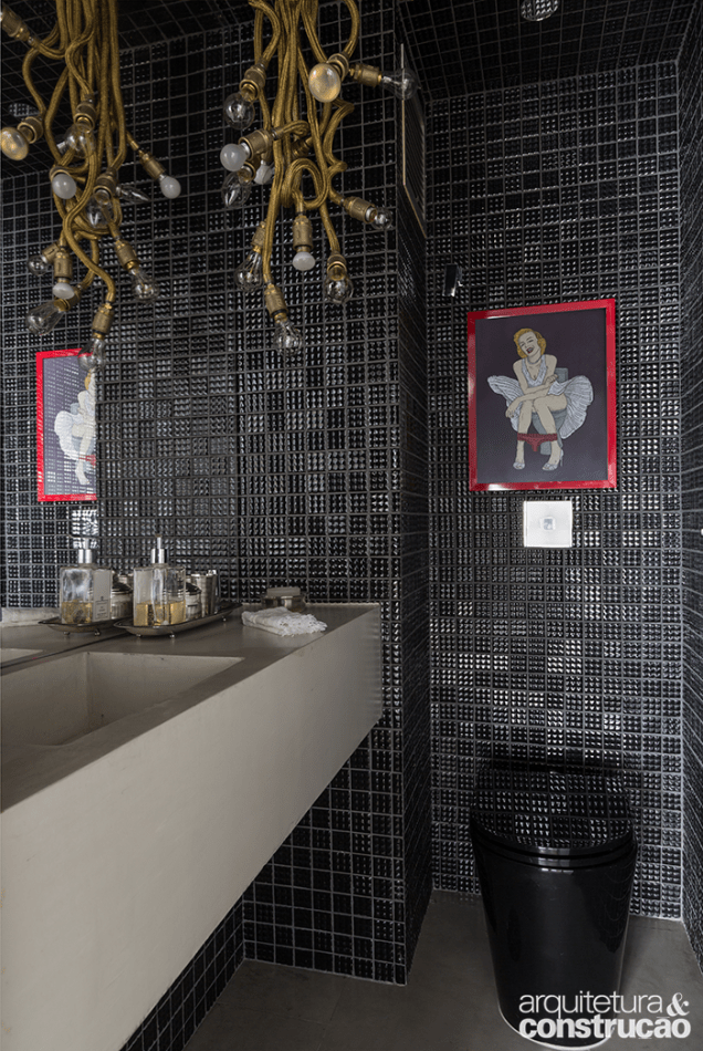 Tons escuros são predominantes no banheiro que traz elementos divertidos como a ilustração emoldurada sobre a bacia sanitária