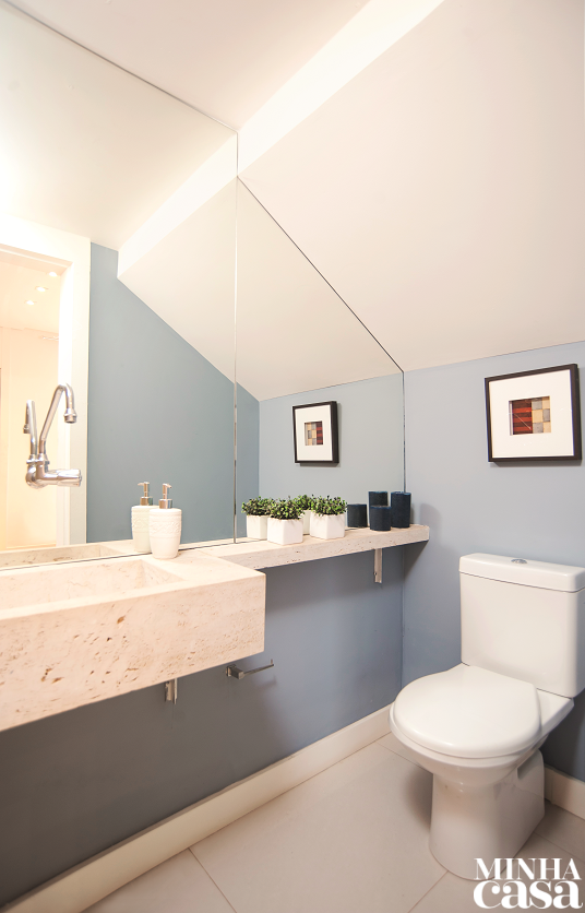 O pequeno lavabo sob a escada ganhou destaque com a pintura delicada (Azul Oxford, ref. 10BB 40/090, da Coral) – como trata-se de um banheiro de visitas, a cor foi pinçada da paleta da ala social. Placas de espelho, acompanhando o recorte do cômodo, ampliam visualmente a área de 1,65 m². Projeto Paula Gambier.