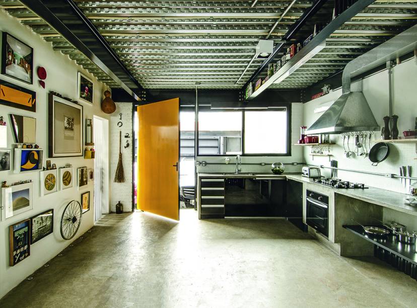 A bancada de concreto em L, feita ao final da obra, acomoda cuba, cooktop a gás e forno elétrico. O mesmo material reveste o piso do térreo, da cozinha ao estar. À esq., atrás de paredes recheadas de arte e achados, ficam: lavabo, dispensa e banheiro de serviço.
