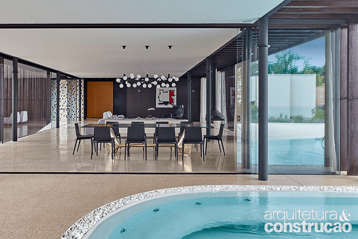 A piscina curva, revestida internamente de tinta epóxi branca, adentra a sala. Repare como as colunas metálicas ficam sempre à vista, opção do projeto.
