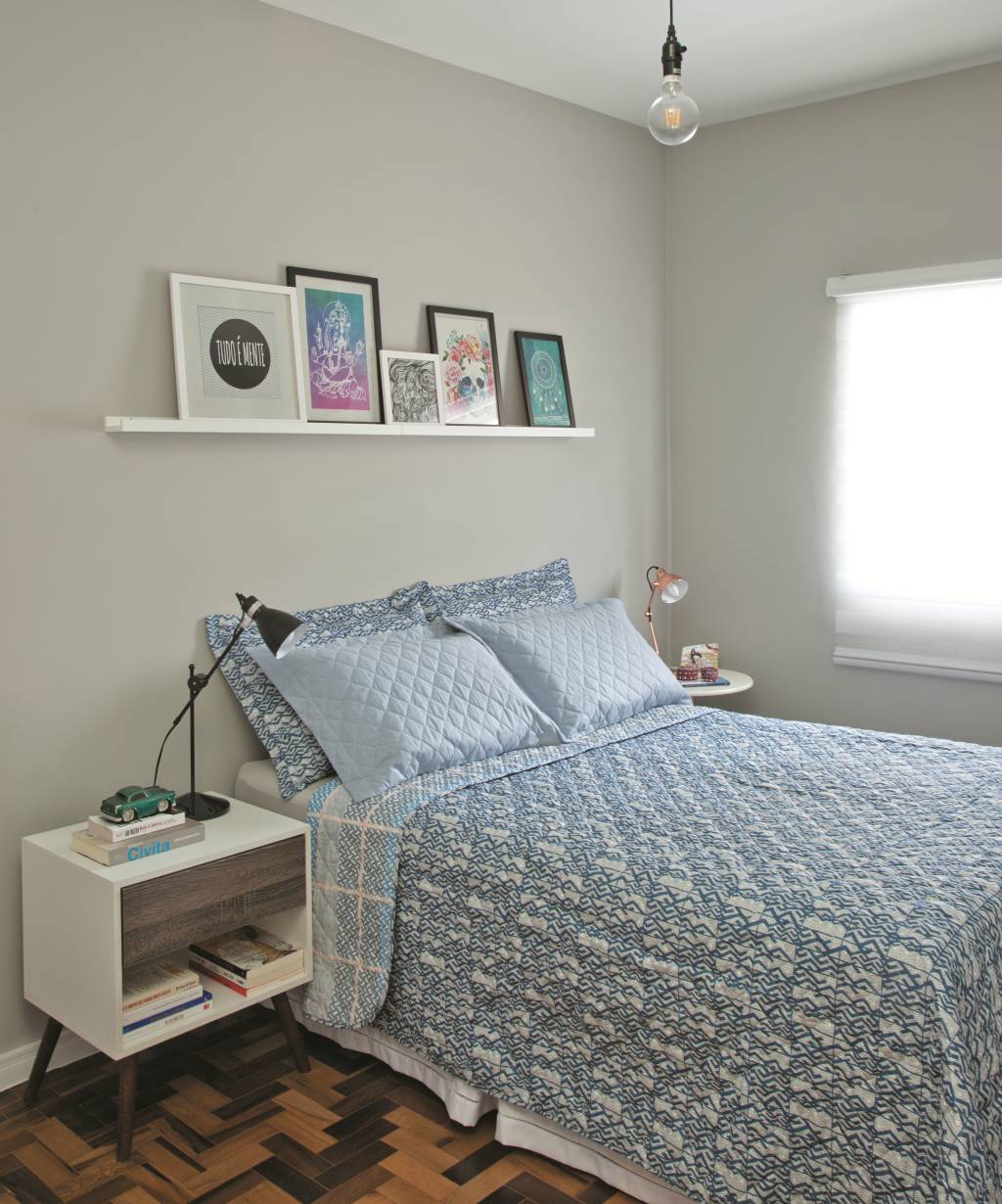 <span>Um tom neutro de prata nas paredes destaca os quadros coloridos apoiados na prateleira.&nbsp;</span><span>Nas laterais da cama, a moradora seguiu a tend&ecirc;ncia de criados-mudos descombinados, com lumin&aacute;rias tamb&eacute;m diferentes.</span>