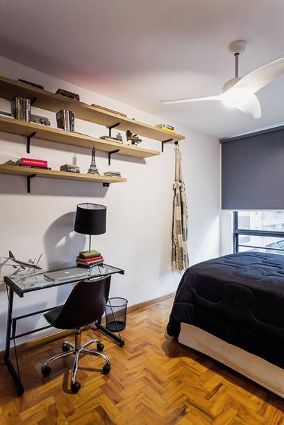 Na parede lateral do quarto, o designer projetou prateleiras suspensas, presas por mãos-francesas.