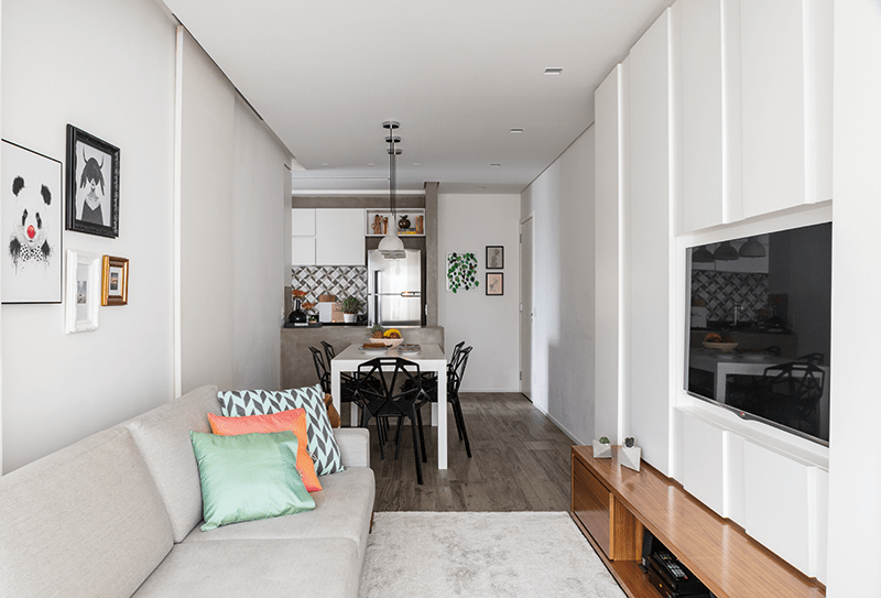 Área social e quartos ganharam porcelanato com aparência de madeira (Emil). No tom da parede, a porta de correr (à esq., na foto) fica imperceptível. A estante de MDF pintado esconde o shaft de água pluvial do edifício (a primeira coluna, na foto abaixo