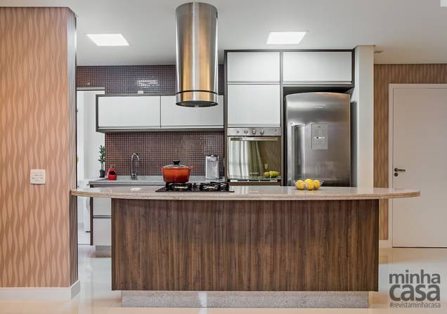 A cozinha é integrada ao estar, mas, no lugar da bancada que faria a divisão dos ambientes, há uma verdadeira ilha gourmet - com direito a cooktop, espaço para as visitas se reunirem em torno do chef e práticos gavetões sob o tampo ovalado. A reforma, comandada pela designer de interiores Leticia Merizio, de São Paulo, pediu adaptações nos encanamentos: foi preciso prever a mudança do ponto de gás para instalar o fogão de mesa e rebaixar o teto com gesso para ligar a coifa. Seguindo a linguagem da sala, a alvenaria da ilha é revestida de laminado no padrão nogueira. Acima da pia, destacam- se pastilhas de vidro (2,30 x 2,30 cm), na cor Rosa Antigo, da Cecrisa, e marcenaria encomendada sob medida. A cozinha é integrada ao estar, mas, no lugar da bancada que faria a divisão dos ambientes, há uma verdadeira ilha gourmet - com direito a cooktop, espaço para as visitas se reunirem em torno do chef e práticos gavetões sob o tampo ovalado. A reforma, comandada pela designer de interiores Leticia Merizio, de São Paulo, pediu adaptações nos encanamentos: foi preciso prever a mudança do ponto de gás para instalar o fogão de mesa e rebaixar o teto com gesso para ligar a coifa. Seguindo a linguagem da sala, a alvenaria da ilha é revestida de laminado no padrão nogueira. Acima da pia, destacam- se pastilhas de vidro (2,30 x 2,30 cm), na cor Rosa Antigo, da Cecrisa, e marcenaria encomendada sob medida.