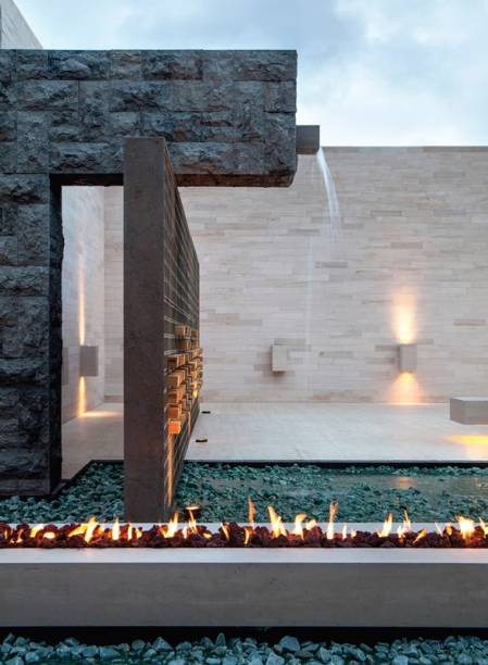 Nem sob chuva e vento a lareira idealizada por Guilherme Torres apaga ou deixa de aquecer o espaço ao ar livre. Embutidos na estrutura de limestone (0,25 x 0,60 x 6 m) e disfarçados por pedras vulcânicas, os quatro kits a gás (Construflama) possuem tecnologia digital que garante o funcionamento seguro nessas condições. “Posso ligar todos ou apenas um módulo e obter diferentes efeitos”, diz o arquiteto. Graças à faixa preta pintada na base, o bloco de pedra parece solto do piso.