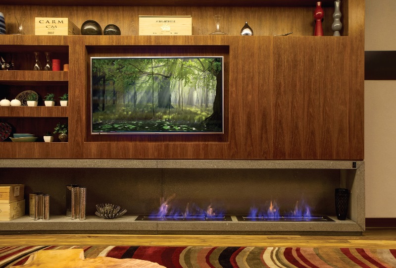 Se faltar espaço na sala, por que não inserir a lareira num móvel que acumule também TV e estante? Nesta ideia do arquiteto Gustavo Paschoalim, o painel de cumaru com 2,75 m de comprimento e 4,20 m de altura tem profundidade de 42 cm, determinada pelos dois modelos de aço inox da Largrill, de 0,26 x 1,20 m cada um. Alimentados com álcool gel 80º, eles aquecem uma área de 100 m² ao redor. Precisaram apenas ser previstos na caixa de granito preto são gabriel. “É uma pedra barata e resistente para esse uso. Com o acabamento jateado fosco, ganhou nobreza e um tom acinzentado”, ensina.
