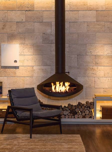 Sobre o aparador de laca, projetado pela arquiteta carioca Paola Ribeiro, a lareira suspensa Tarus (Construflama), a álcool de cereais, marca presença diante da parede revestida de travertino. “Seu traçado escultórico arremata o estilo contemporâneo do ambiente”, enfatiza. De aço corten, a peça com abertura de 1 m não toma espaço e se alia aos matizes terrosos do lugar. Também pode ser executada na versão giratória, com duas bocas, e à lenha ou a gás.