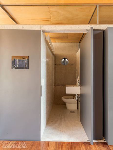O vão envidraçado de 40 cm, no alto, fornece luz natural ao lavabo, revestido de pastilhas de vidro branco. A ventilação se dá através da escotilha na parede de concreto. “Recortamos a divisória com uma máquina e encaixamos ali a portinhola de chapa de ferro pivotante”, explica Fernando Viégas, do Una Arquitetos.