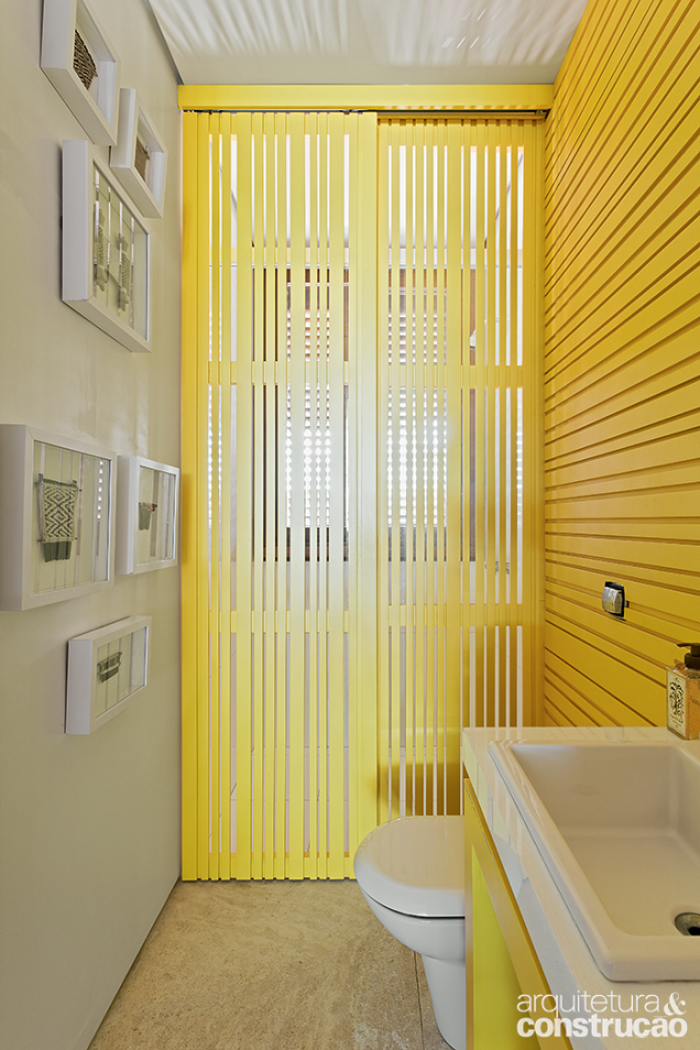 Pinceladas de amarelo colorem este ambiente com dupla função: lavabo e banheiro. A cor está presente no revestimento de madeira e também na divisória móvel que isola a área do chuveiro.