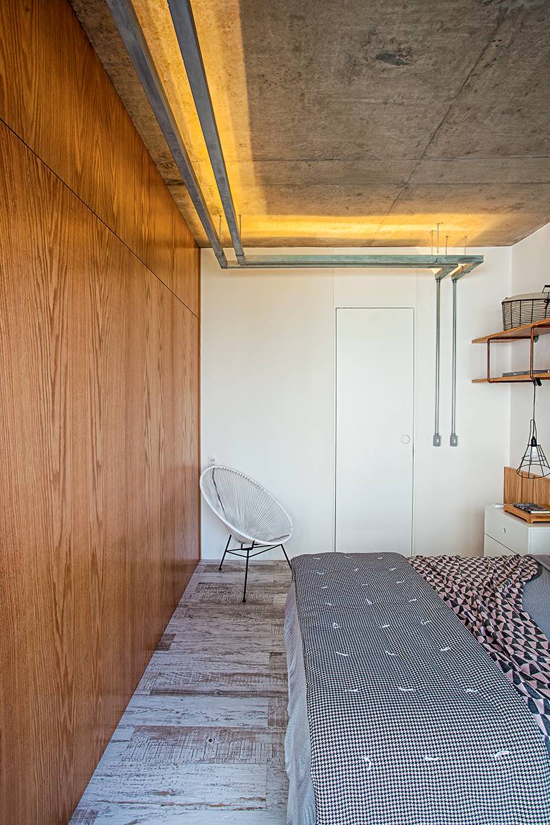 No quarto projetado pelos arquitetos Diogo Luz e Z&eacute; Guilherme Carceles, do escrit&oacute;rio Casa 100, o intuito foi valorizar a textura da laje de concreto. Para isso, usaram duas faixas de eletrocalhas, de 6 m cada uma, fixadas com bra&ccedil;adeiras met&aacute;licas. Dentro delas, colaram fita de led com temperatura de cor 2 700 K (Lustres Yamamura). Na lateral da cama, a lumin&aacute;ria (Tok&Stok) recebeu l&acirc;mpadas led comuns. Produ&ccedil;&atilde;o visual: Nuria Uliana.