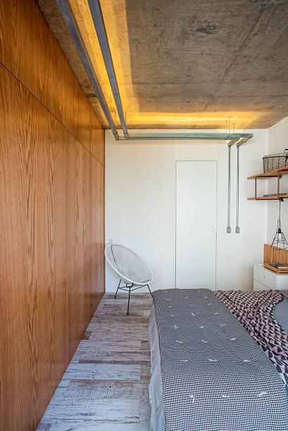 No quarto projetado pelos arquitetos Diogo Luz e Zé Guilherme Carceles, do escritório Casa 100, o intuito foi valorizar a textura da laje de concreto. Para isso, usaram duas faixas de eletrocalhas, de 6 m cada uma, fixadas com braçadeiras metálicas. Dentro delas, colaram fita de led com temperatura de cor 2 700 K (Lustres Yamamura). Na lateral da cama, a luminária (Tok&Stok) recebeu lâmpadas led comuns. Produção visual: Nuria Uliana.