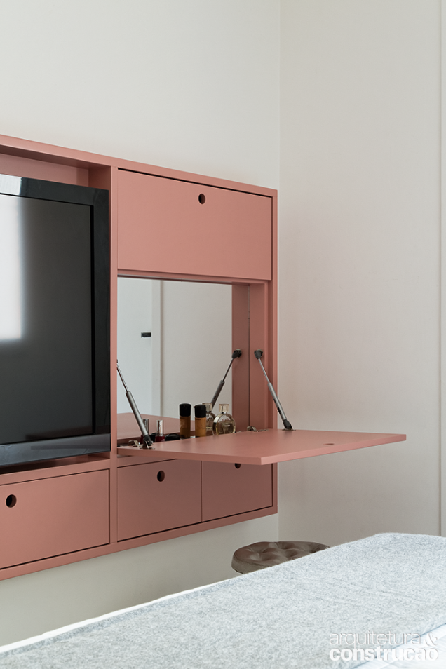 O painel da TV também é uma penteadeira com quatro nichos fechados por portas basculantes. Com 10 cm de profundidade, exibe laca rosa no acabamento.