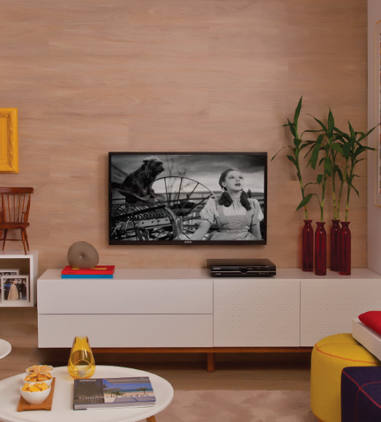 Para comemorar o quarto aniversário da revista (edição nº 49, maio/2014), as designers de interiores Bianca Notari e Ana Claudia Costa, de São Paulo, idealizaram uma sala que segue a receitinha infalível: base neutra e pitadas alegres de cor. Em vez de lançar mão de um painel tradicional, a sacada da dupla foi cobrir a parede da TV com o mesmo revestimento vinílico do piso (padrão Fava, da linha Essence Liso, da Tarkett Fademac. Leroy Merlin, R$ 57,90 o m²). “É um acabamento que tem bom preço, não risca e apresenta um aspecto bem próximo ao da madeira natural”, justifica Bianca. De acordo com o fabricante, tanto é possível fixar as réguas diretamente na parede quanto sobre uma chapa de MDF – em ambos os casos, a instalação deve ser feita com cola de contato sem toluol.