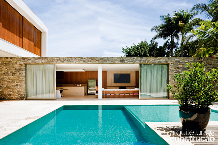 O bloco de lazer reúne área de refeições, sala de TV, brinquedoteca e até adega. Assim como acontece no estar, esse espaço volta-se para a piscina, revestida de pastilhas de 2,5 x 2,5 cm da Bisazza (Vallori), com piso de travertino romano bruto ao redor (Silestone de Brasília) e deck de ipê (Talentus Esquadrias).