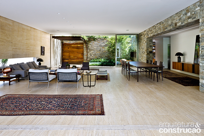 Um jardim compacto funciona como hall da casa, com o paredão da fachada revestido de pedra moledo, boa parceira para a madeira de demolição da porta de entrada.