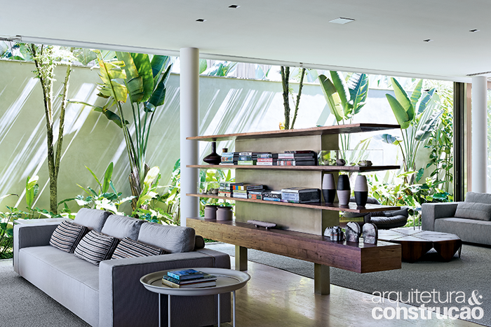 Construída no local, a estante imaginada pelos arquitetos apoia objetos, enfeites e esconde a TV (no verso, dentro do nicho central), definindo o home theater. Repare nos pilares redondos, que não coincidem com o fechamento: as esquadrias (Unibox) correm independentemente. São recolhidas fora da casa, num prolongamento dos trilhos, para evitar obstáculos entre sala e jardim.