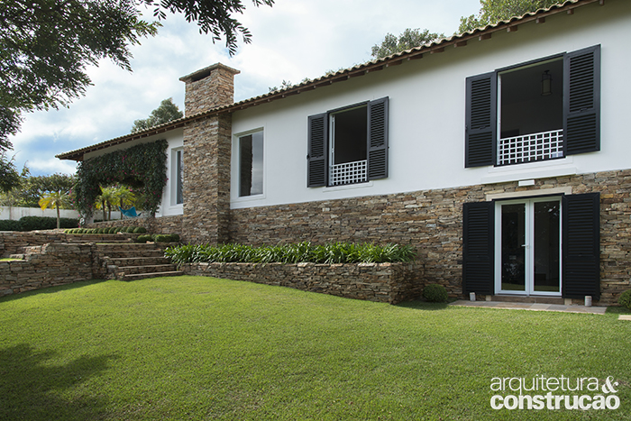 As venezianas pretas marcam uma das fachadas da residência e contrastam com o gradil branco. No declive, no patamar inferior, existe um quarto extra.