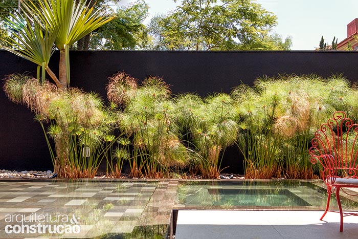 Com área rasa para uma prainha e outra para um spa, a piscina, revestida de pedras vulcânicas (Palimanan), ganhou ares de lago ao refletir a vegetação do entorno e muda de matiz conforme a variação de luz. O verde dos papiros é realçado pela textura preta (Ibratin) do muro. “O paisagismo de Alex Hanazaki tem uma linguagem que completa meu trabalho”, Vanessa Féres, arquiteta.