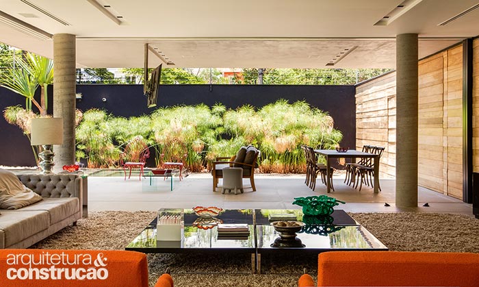 Finalizadas com cera, ripas de freijó (Projearte), presas numa estrutura de sarrafos, preenchem o paredão da sala que segue até o muro externo, ocultando as portas que acessam o hall e a entrada da casa, além da churrasqueira.