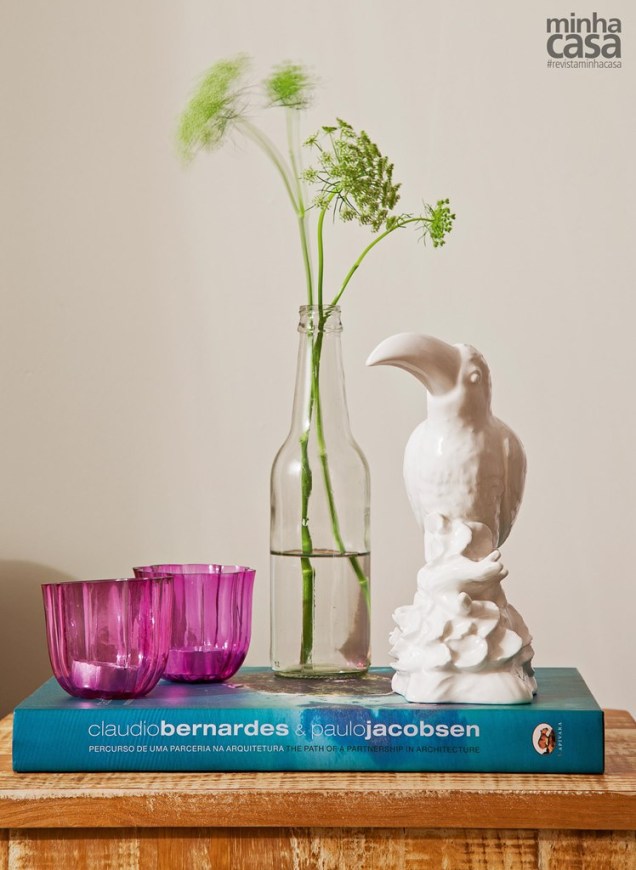 Receita de um arranjo delicado: o livro apoia dois porta-velas de vidro Votive (Etna), garrafinha com ramos de flor de cenoura e tucano de porcelana (Oren).