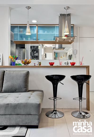 Sala de estar integrada com cozinha e balcão atrás do sofá com banquetas pretas.