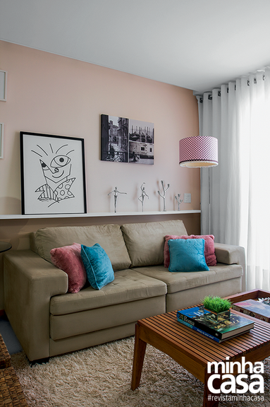 Sala de estar pequena com sofá marrom claro, prateleira acima do sofá com estátuas pequenas e quadro.